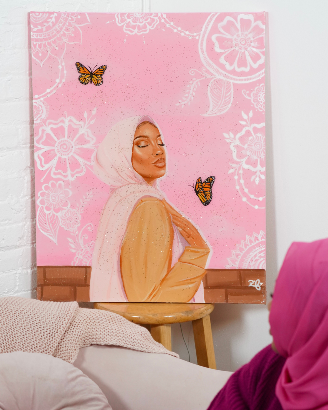 Woman looking at a painting titled 'Her Inner Bliss' by Zeinabou Fatana on a pink background.